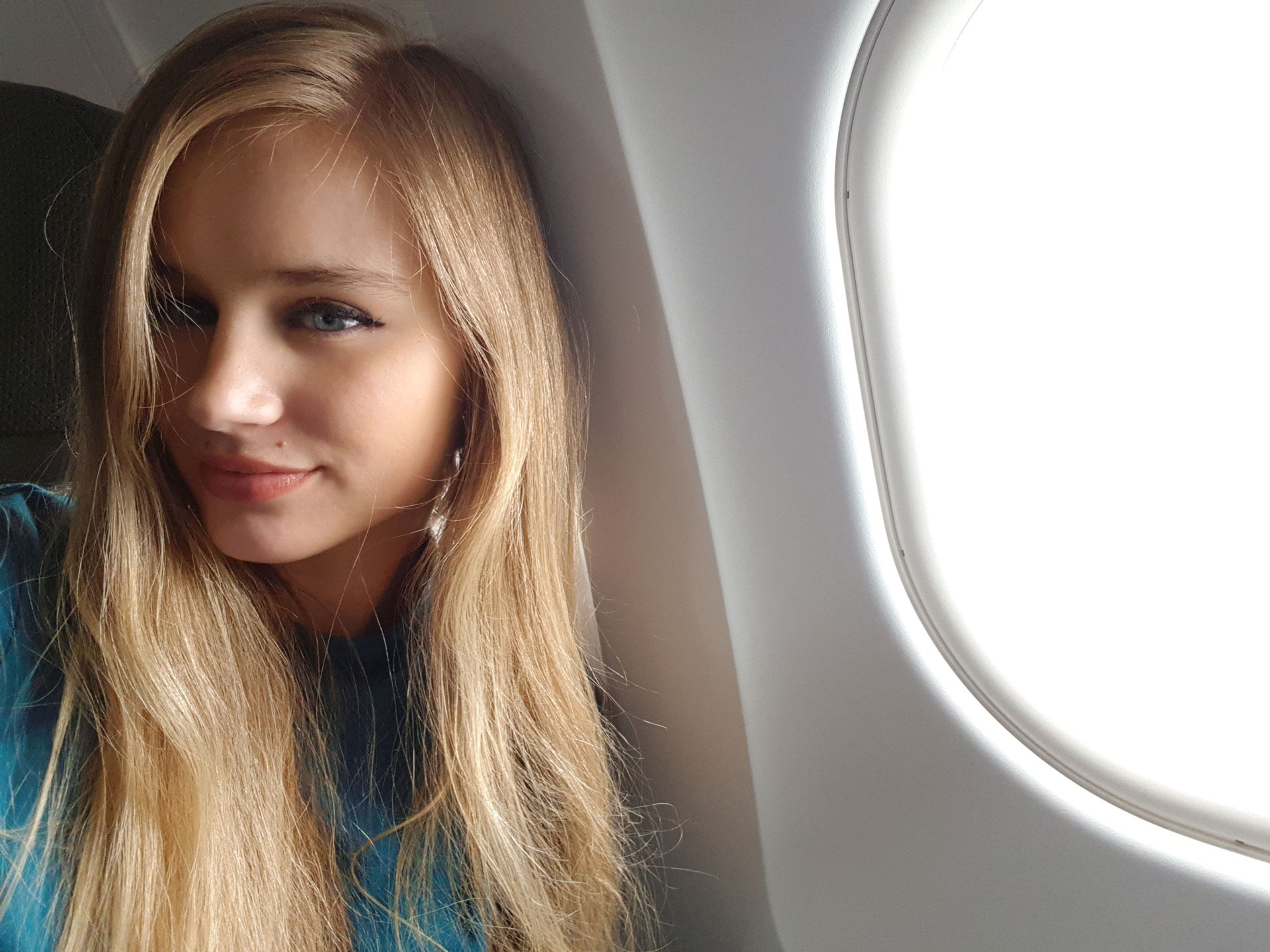 Travel blogger CaliGirlTravelsWorld on airplane at the window seat.