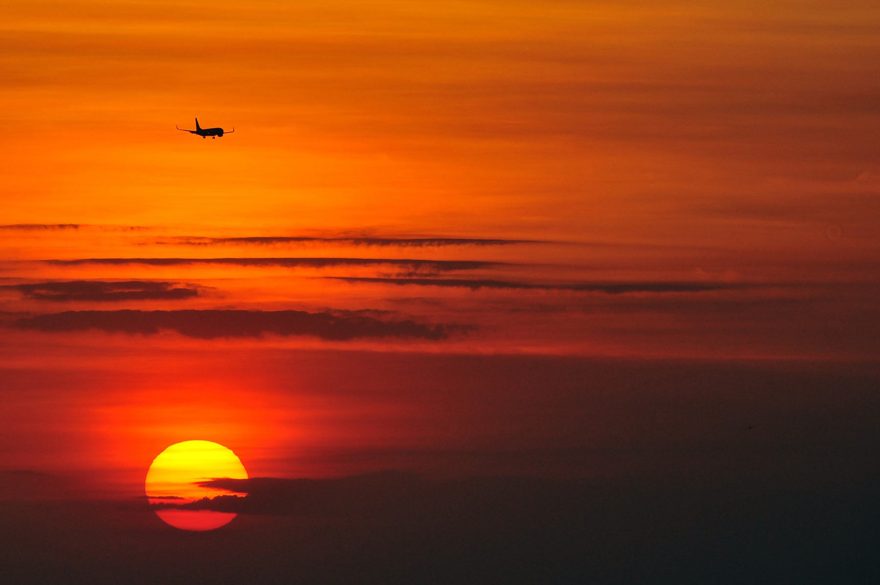 A plane flying over the clouds of a red and orange sunset.